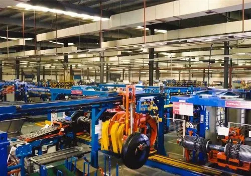 Línea de montaje en una fábrica. Se aprecian maquinaria, neumáticos y piezas mecánicas de color azul. Entorno industrial.