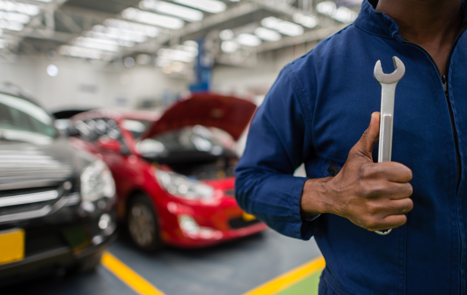A mechanic is holding a wrench in a garage and giving a thumbs up.