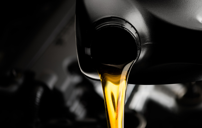 A close up of a bottle of oil being poured into a car engine.