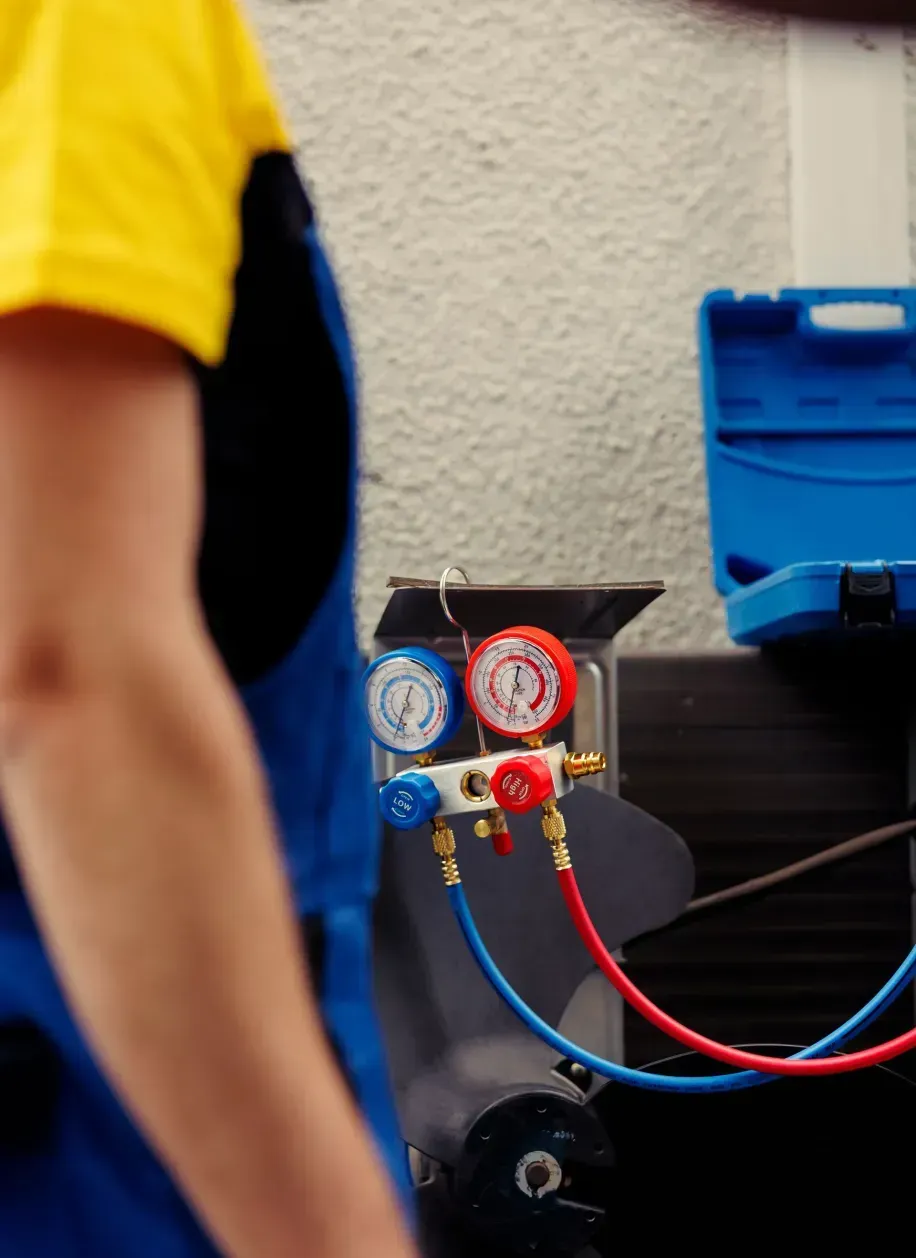 A man in a yellow shirt and blue overalls is working on an air conditioner.