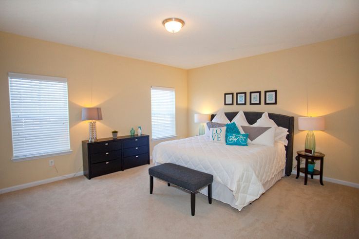 A bedroom with a bed , dresser , lamps and a bench.