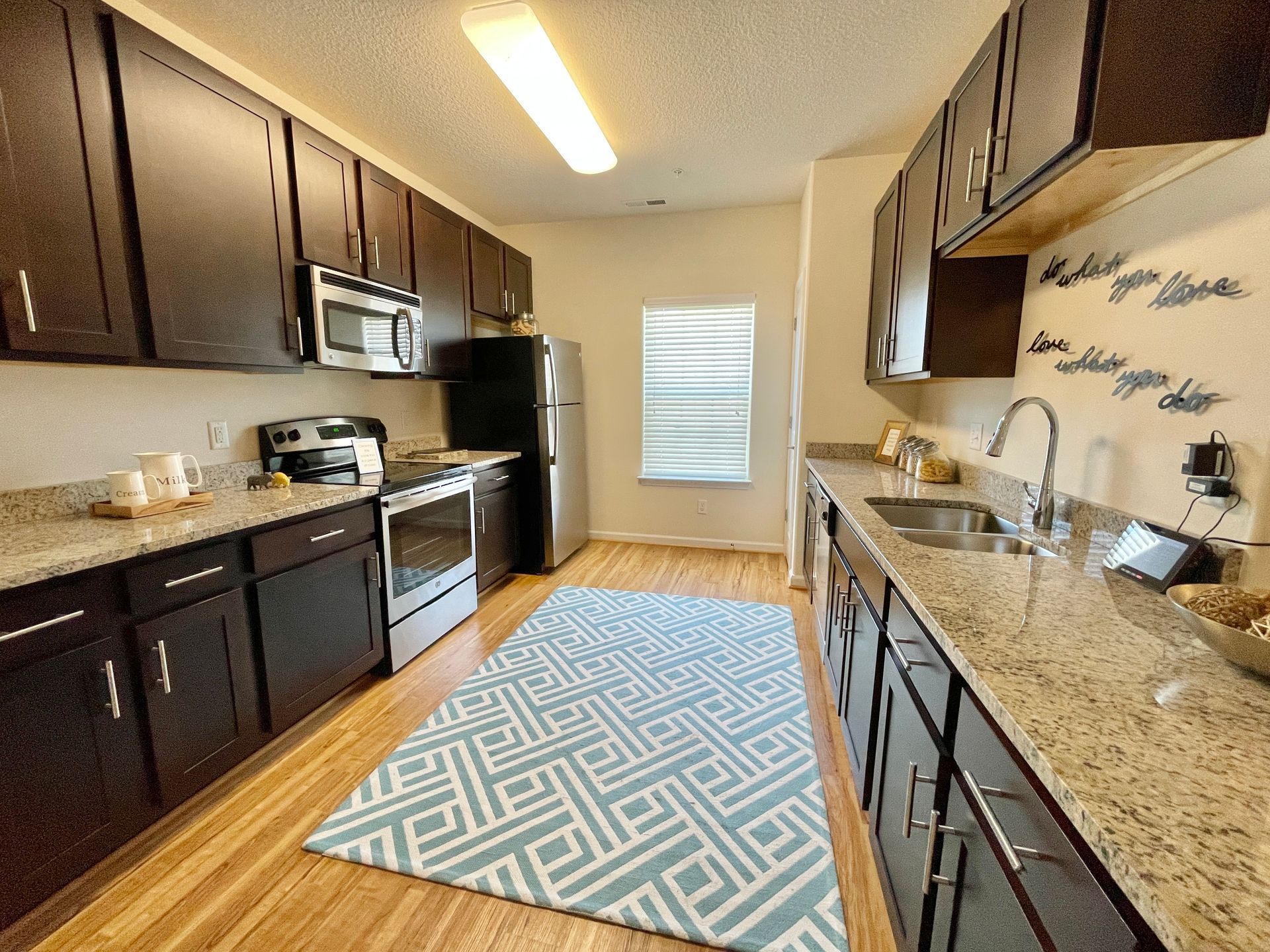 A kitchen with black cabinets , granite counter tops , a rug and a window.