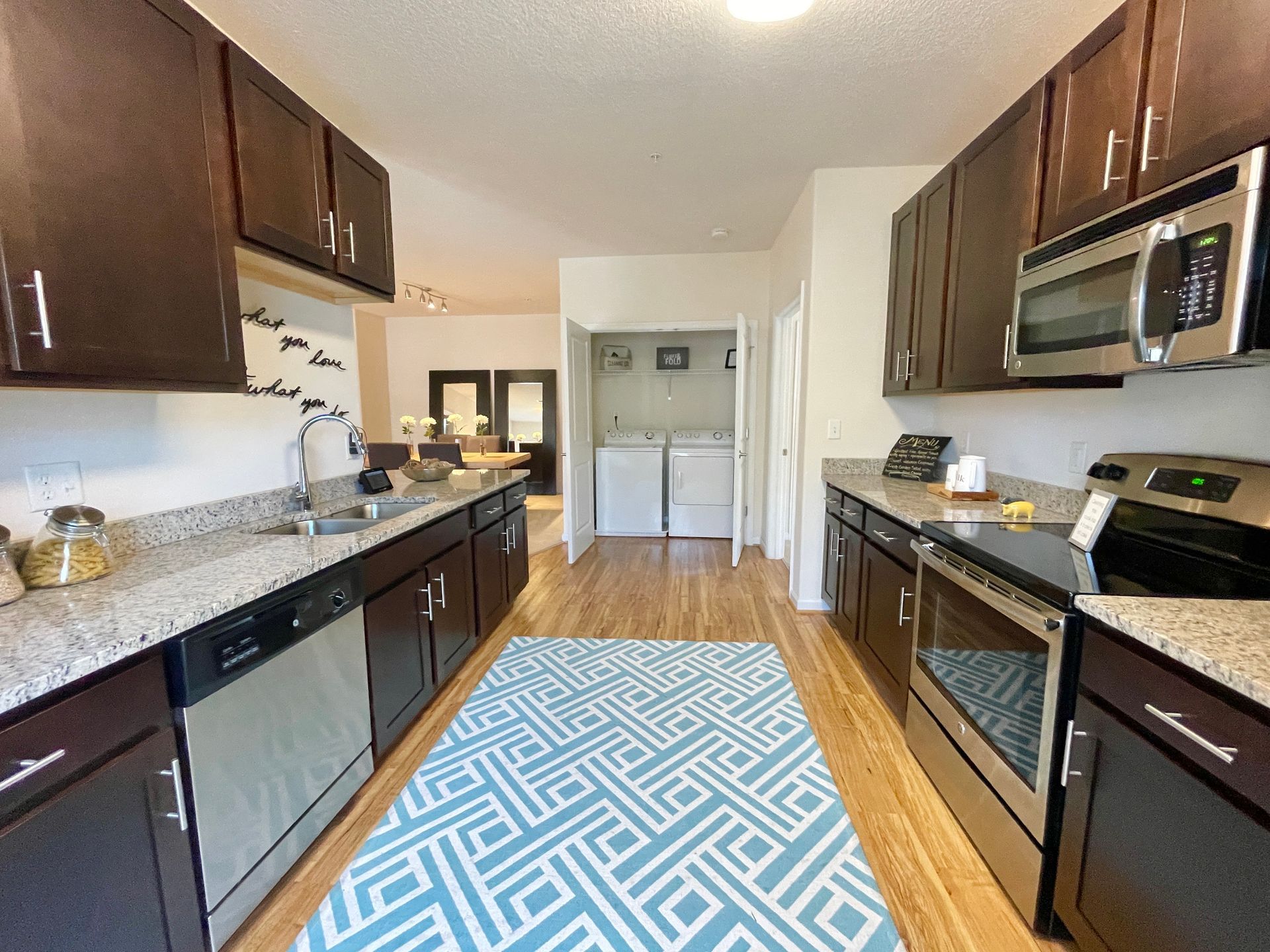 A kitchen with stainless steel appliances and a blue rug on the floor.
