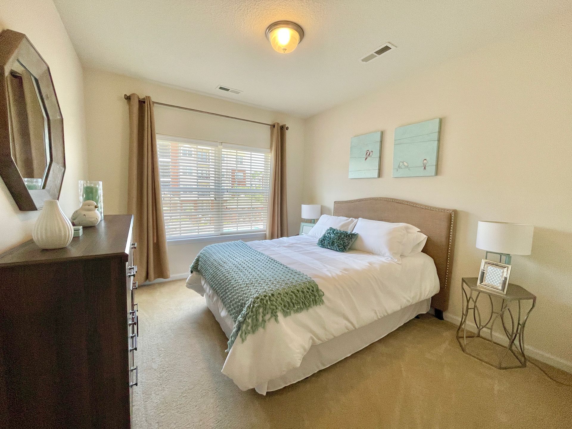 A bedroom with a bed , dresser , nightstand and mirror.