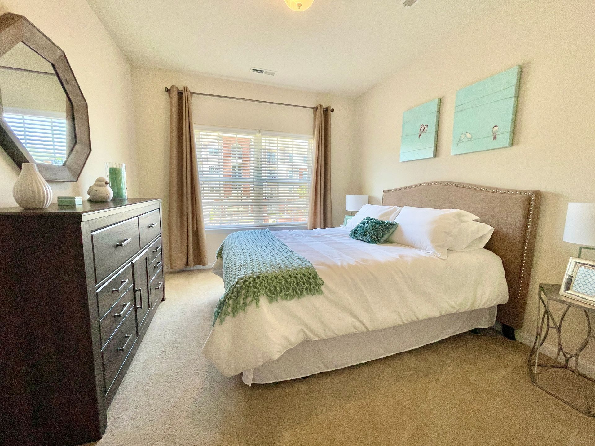 A bedroom with a bed , dresser , mirror and window.