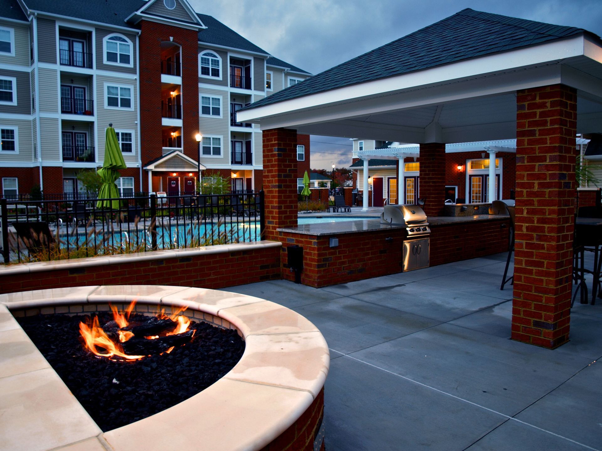 A fire pit in front of a building with a pool in the background