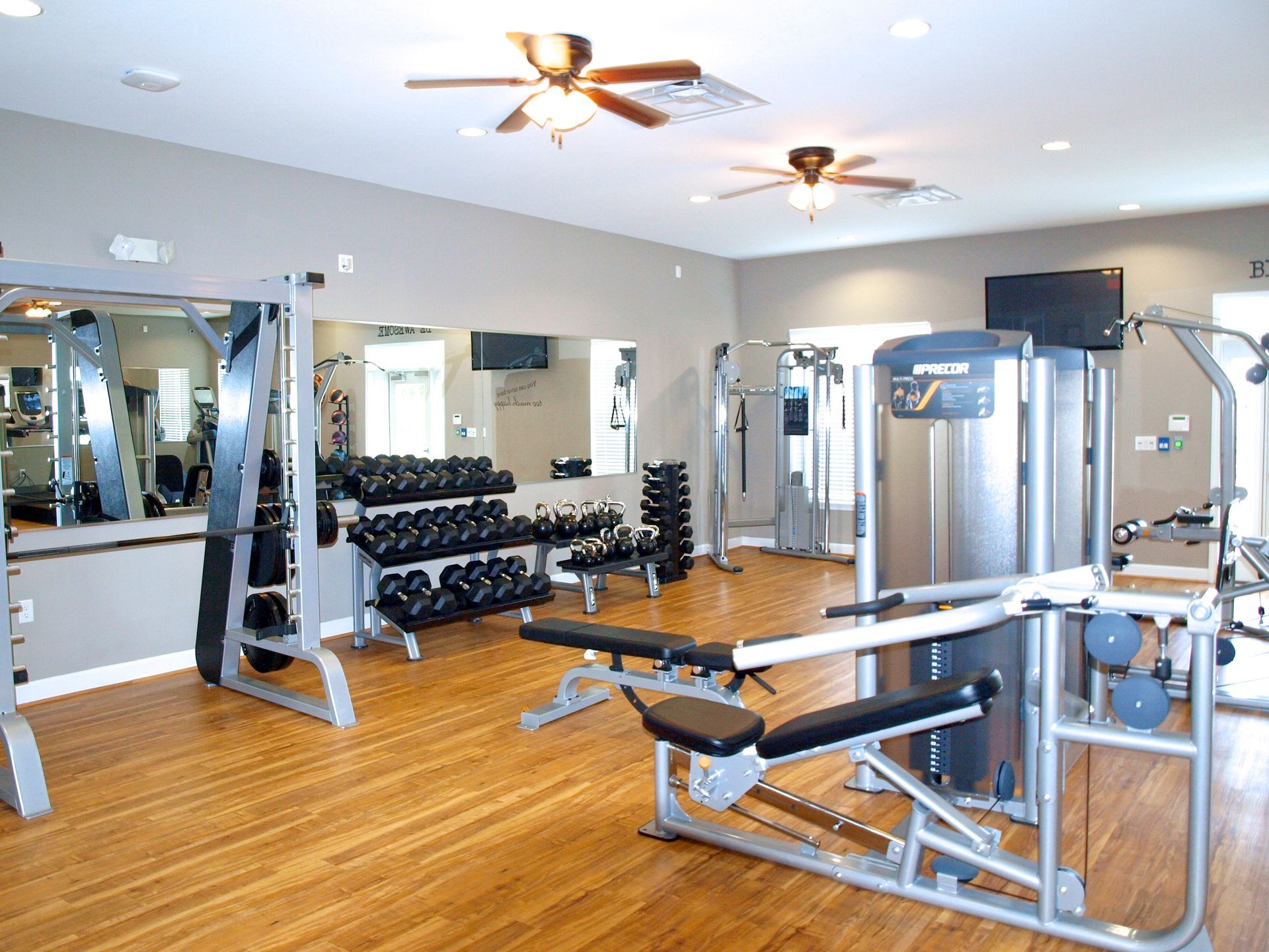 A gym with a lot of equipment and a ceiling fan