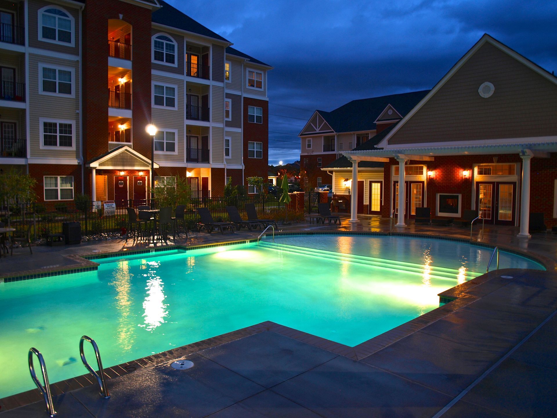 A large swimming pool is lit up at night in front of a building