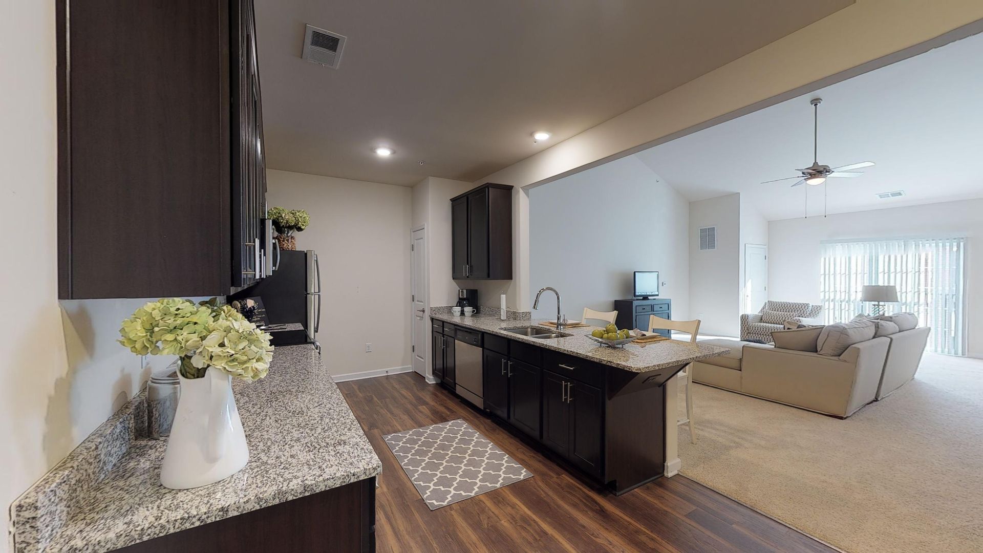 A kitchen with granite counter tops and stainless steel appliances is open to a living room.