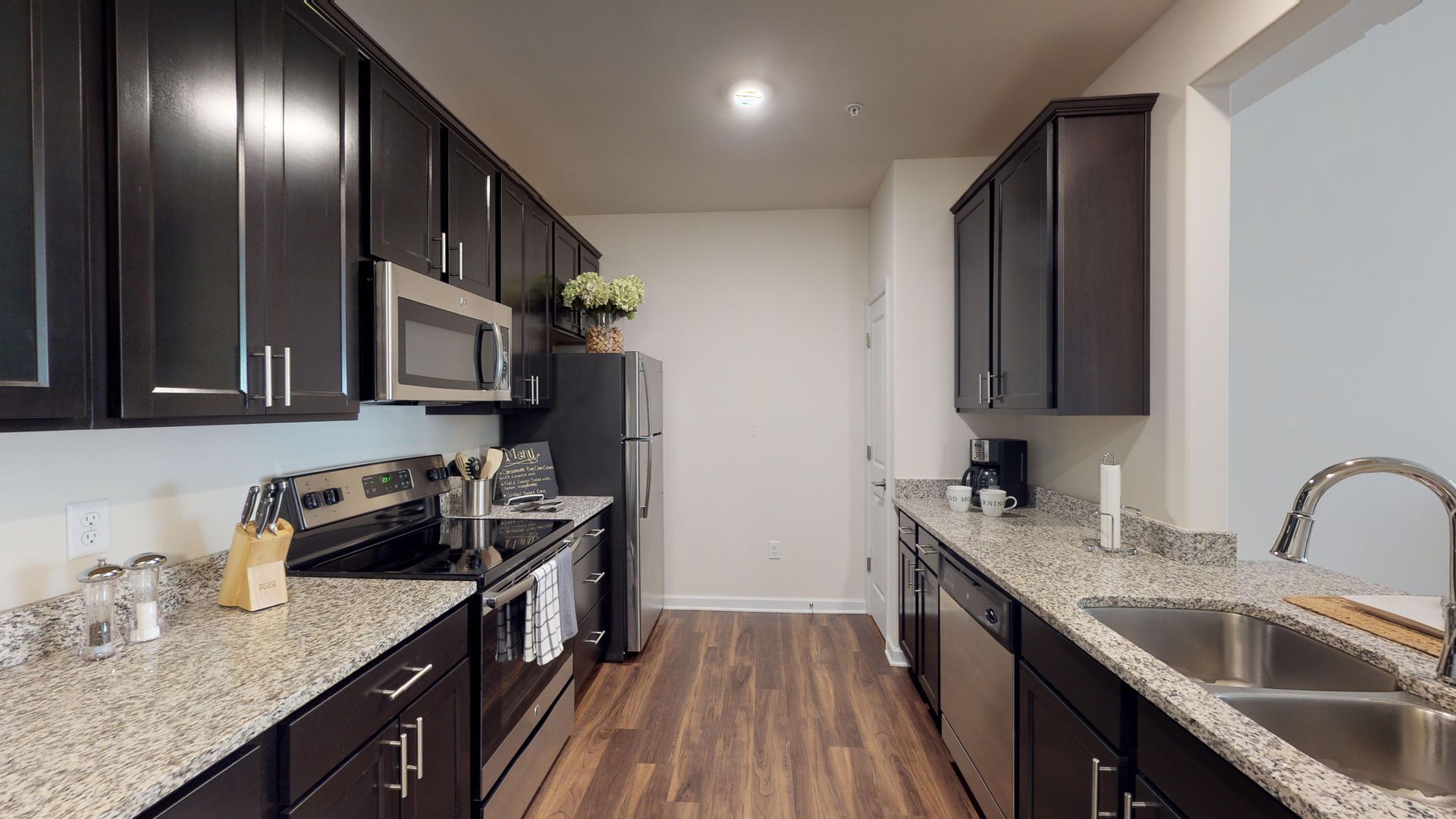 A kitchen with black cabinets , granite counter tops , stainless steel appliances and a sink.