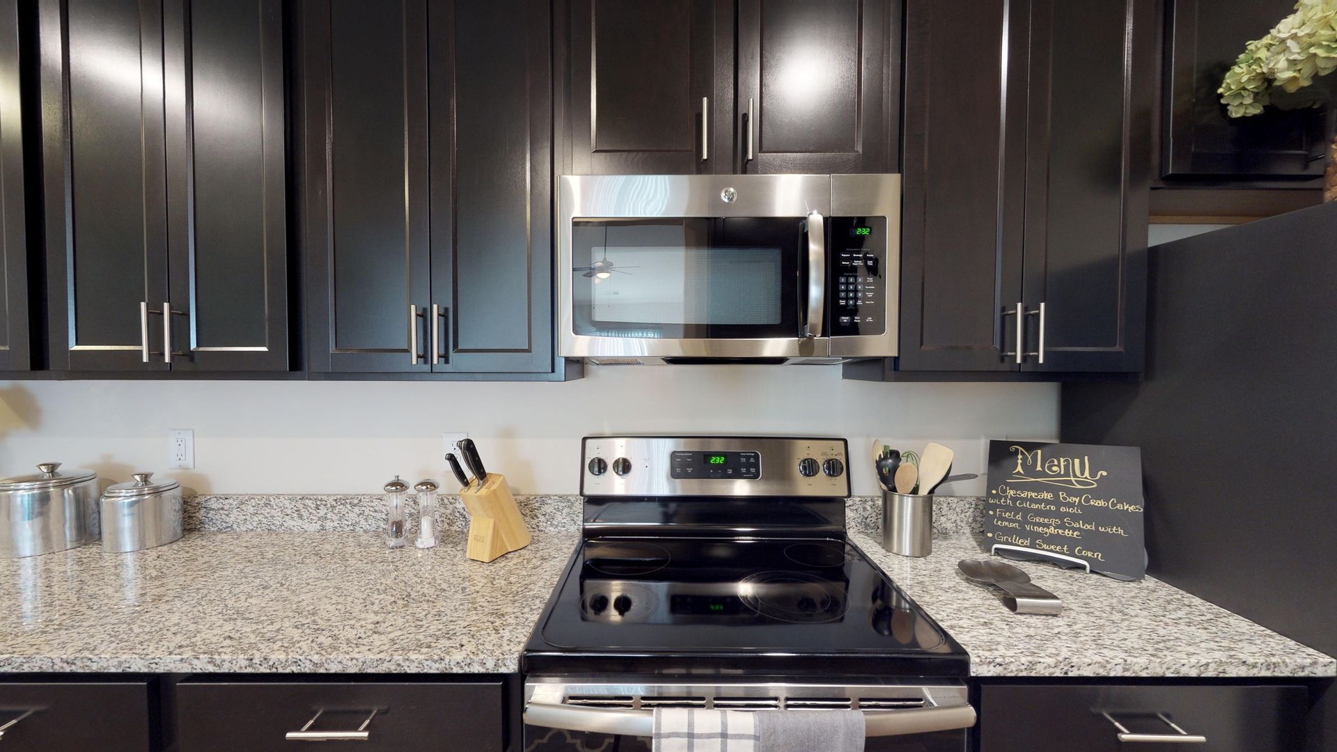 A kitchen with black cabinets , a stove , a microwave , and granite counter tops.