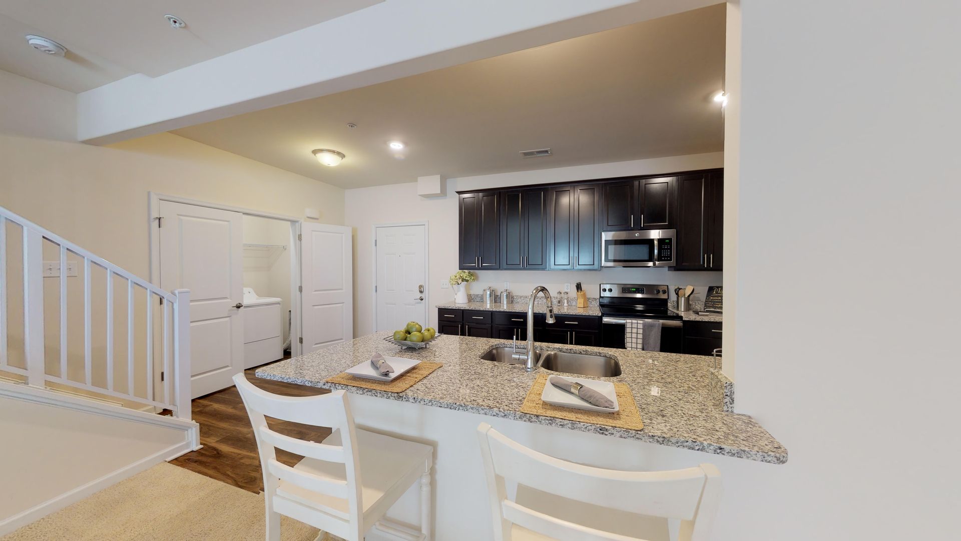 A kitchen with a granite counter top , a sink , a microwave , and a staircase.