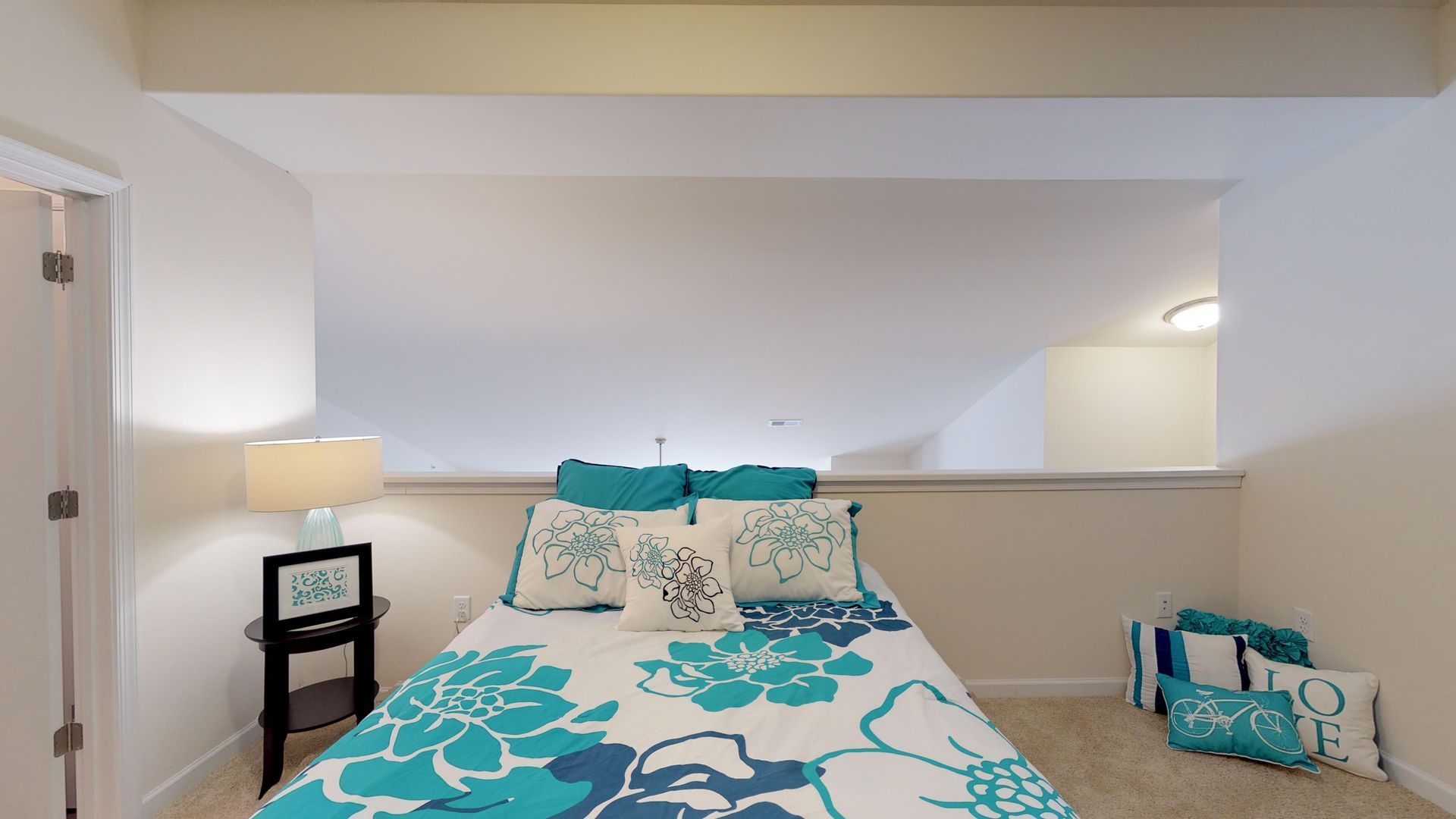 A bedroom with a bed , nightstand , lamp and carpet.