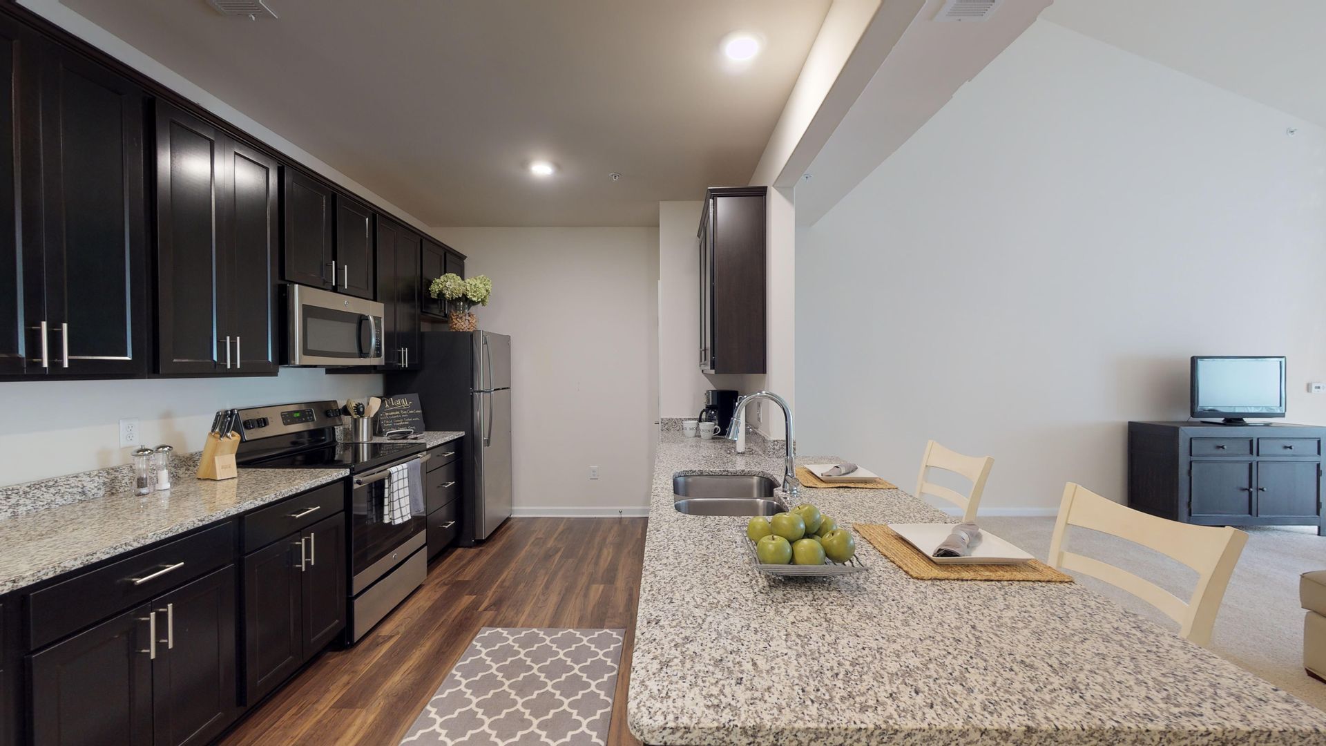 A kitchen with granite counter tops , black cabinets and stainless steel appliances.