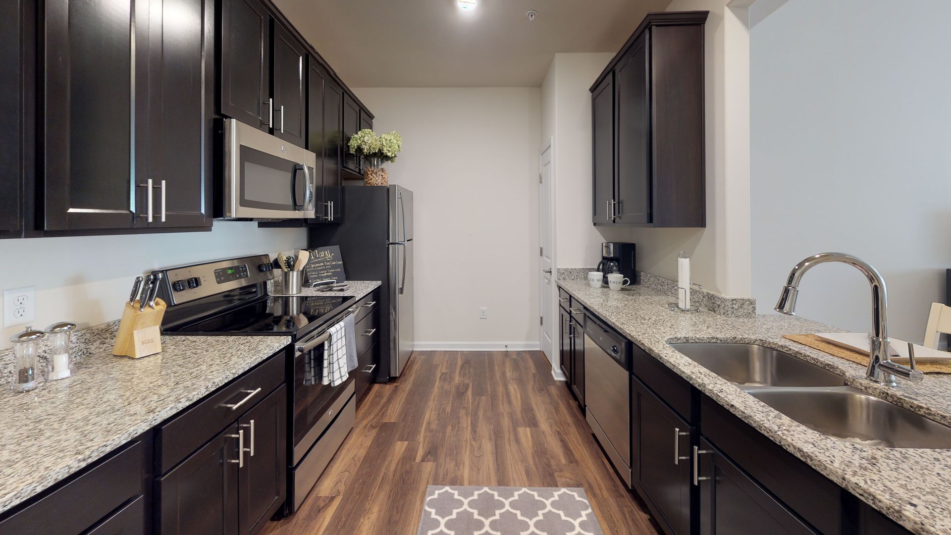 A kitchen with stainless steel appliances , granite counter tops , and black cabinets.