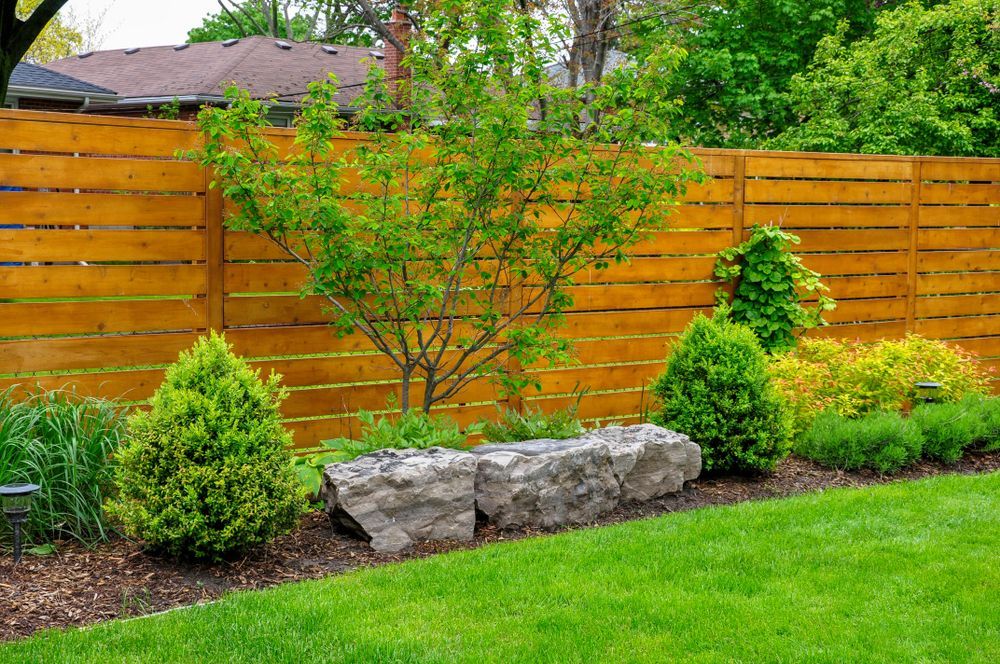 Backyard garden with wood fence, stone bench, and green shrubbery.