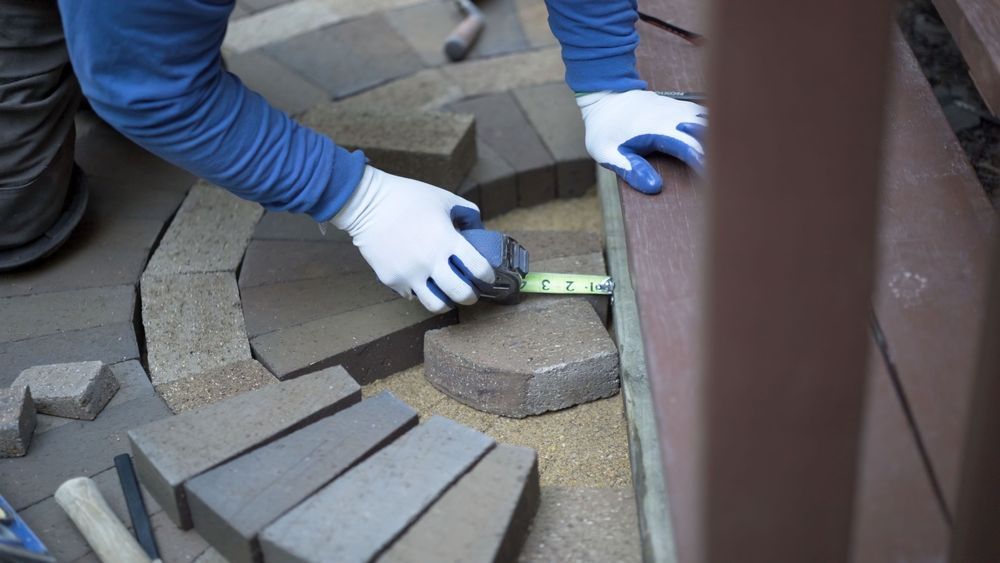 Person wearing gloves measuring pavers next to a wooden border.