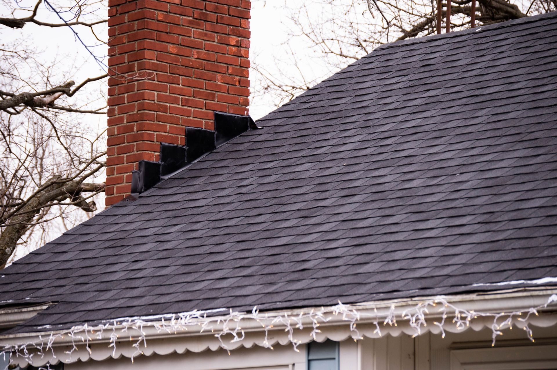 Dark shingled roof with a brick chimney and decorative gutter.