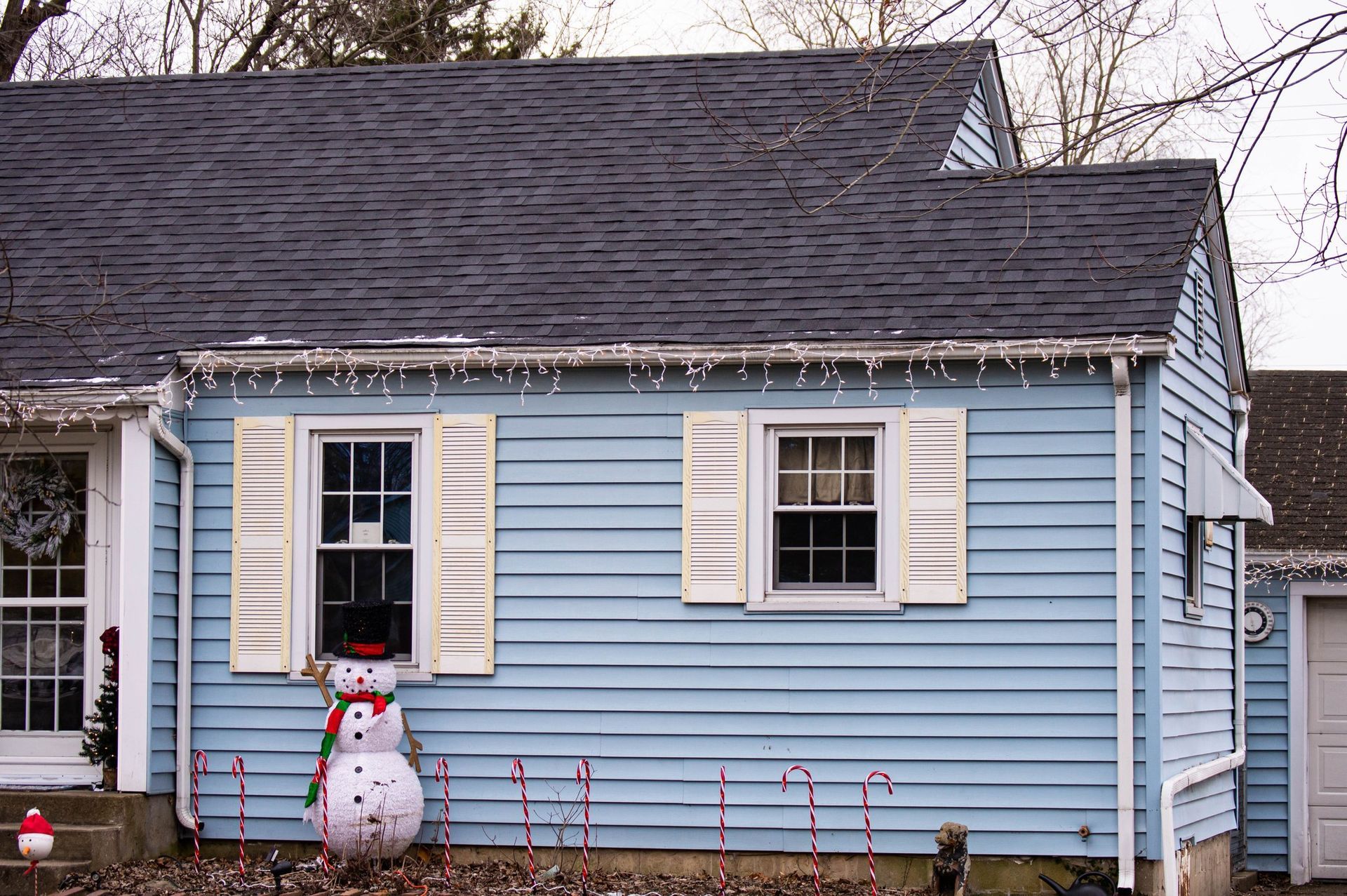 Blue house with white shutters, decorated with Christmas lights and a snowman.