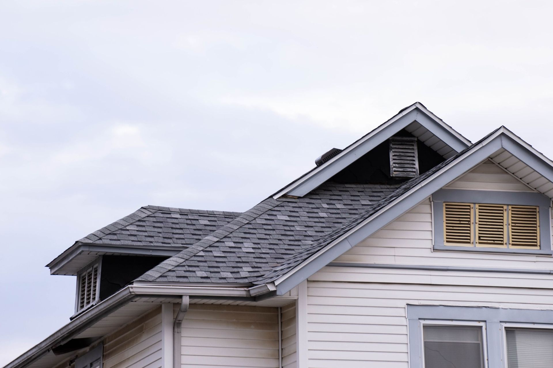 White house with gray roof and blue trim against a cloudy sky.