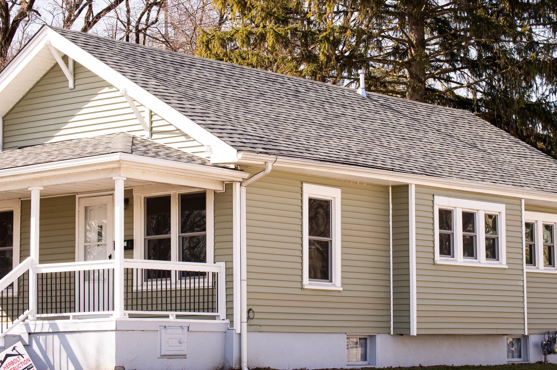 Green house with white trim, porch, and gray shingle roof.