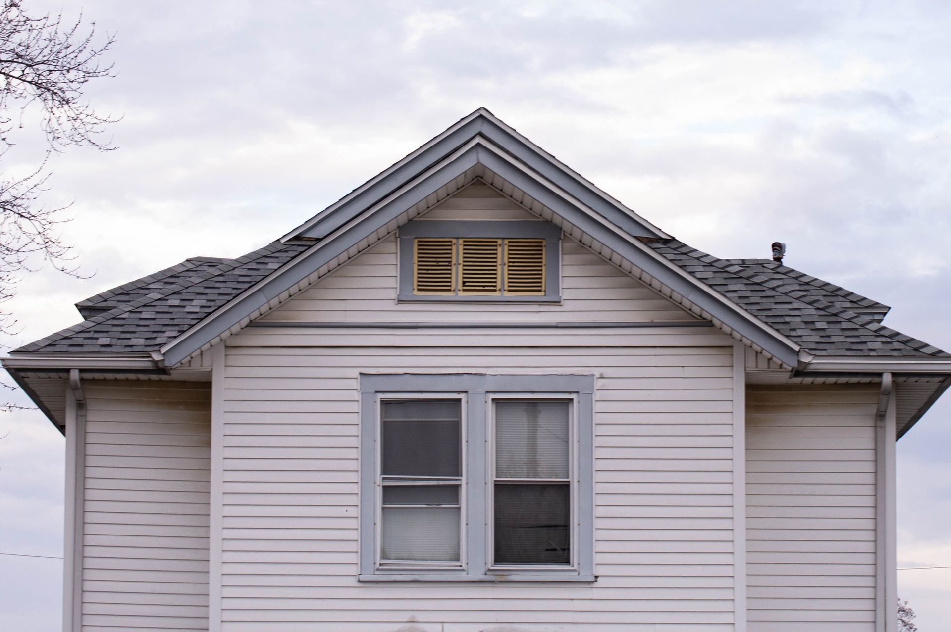 White house with gray trim, two windows on main floor, small window in the peak. Cloudy sky.