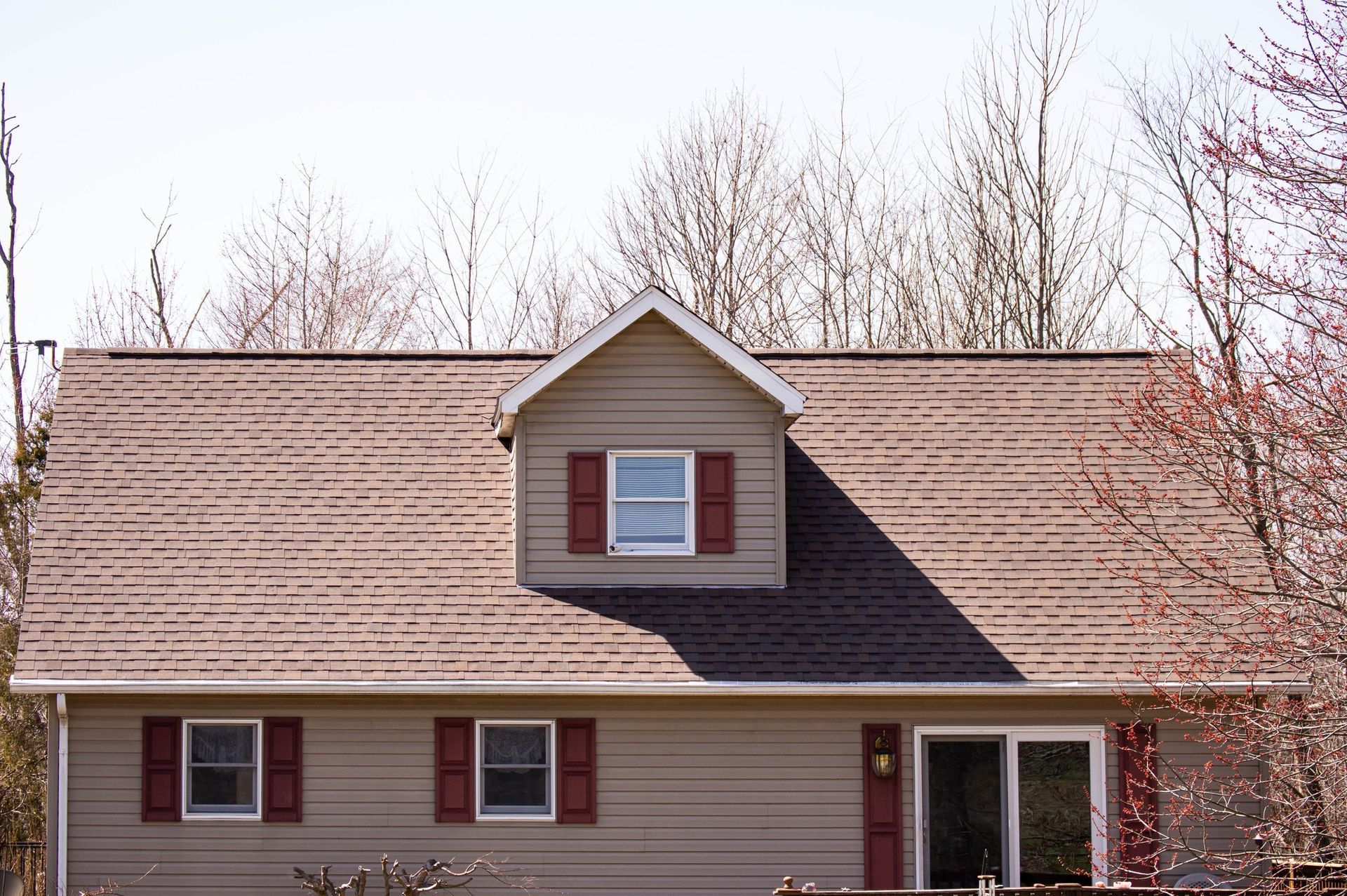 Tan house with brown roof, a dormer, red shutters, and a sliding glass door.