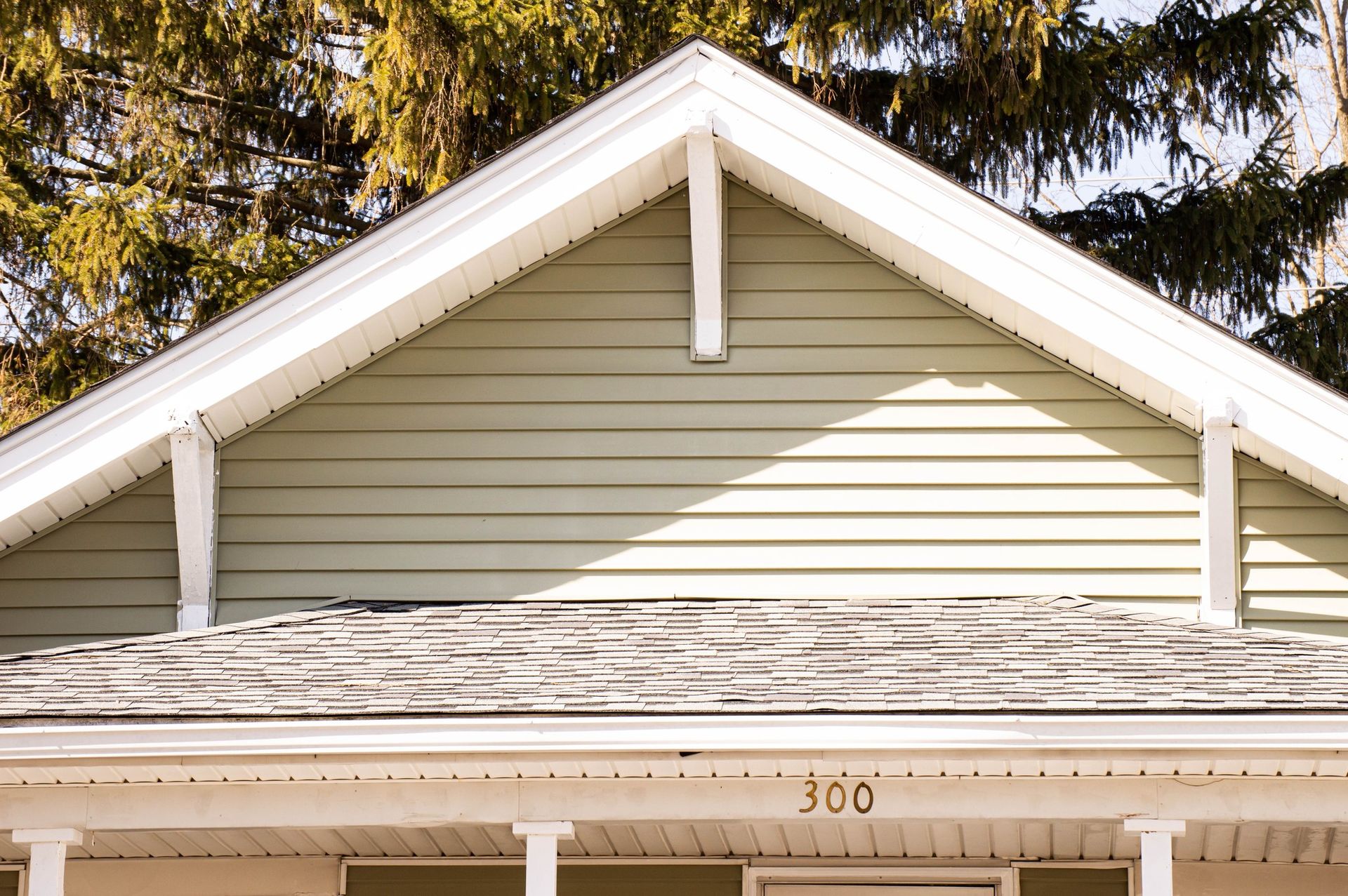 Close-up of a house roof with green siding, white trim, and a number 