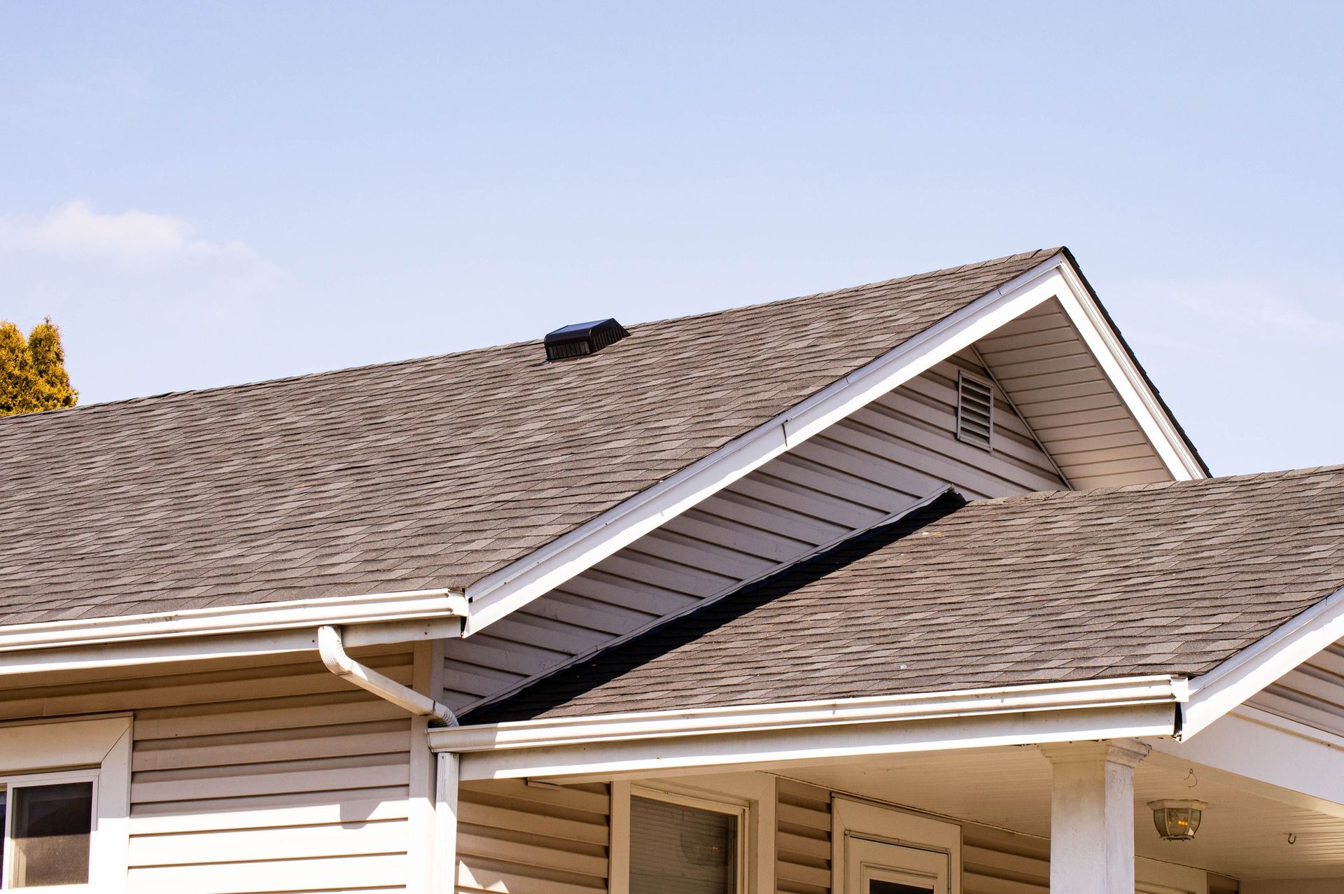 House roof with gray shingles, white trim, and light siding against a blue sky.