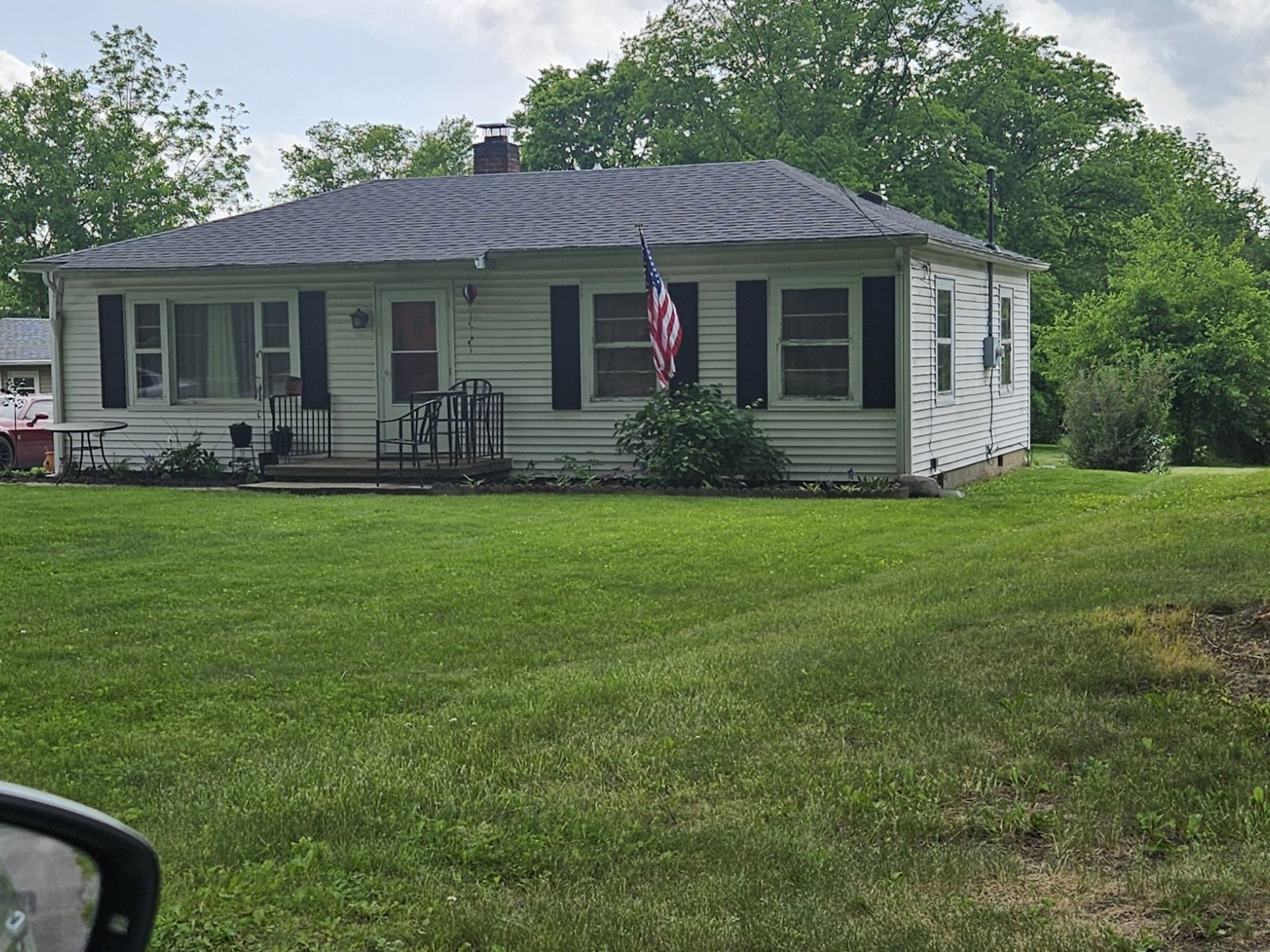 White, one-story house with black shutters, American flag, and green lawn.