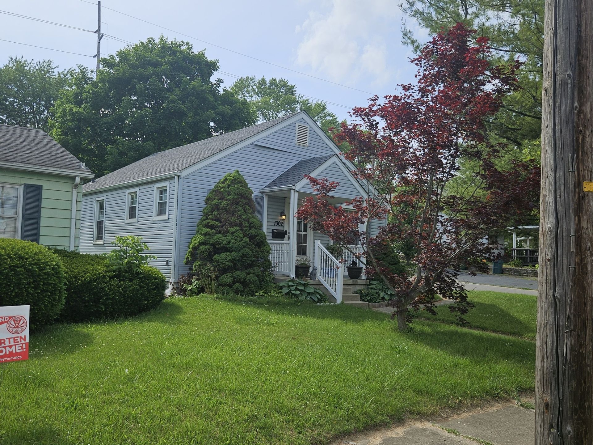 Small blue house with porch, green lawn, red-leafed tree, and power pole.