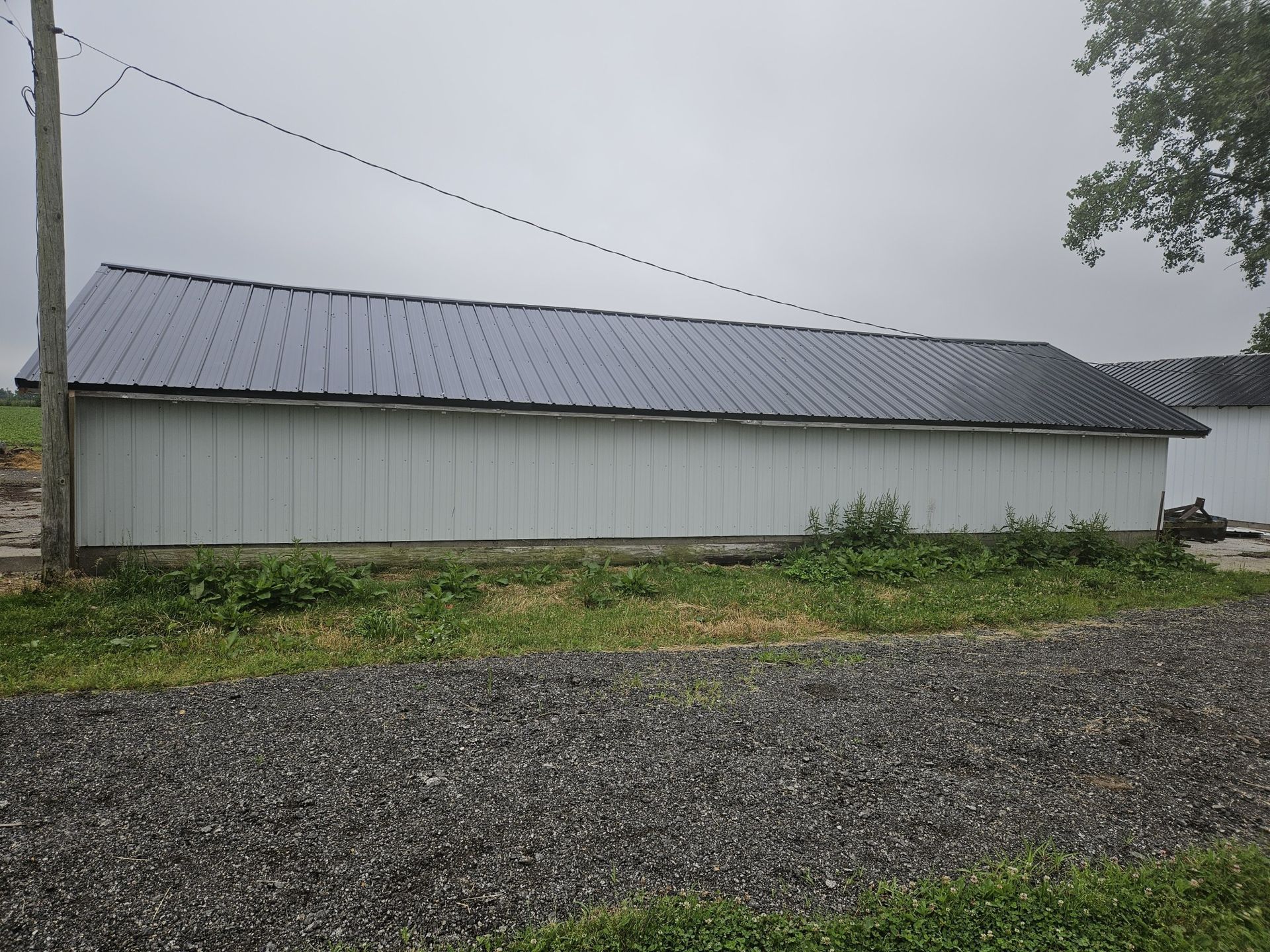 White shed with dark metal roof on a gravel road, overcast sky.