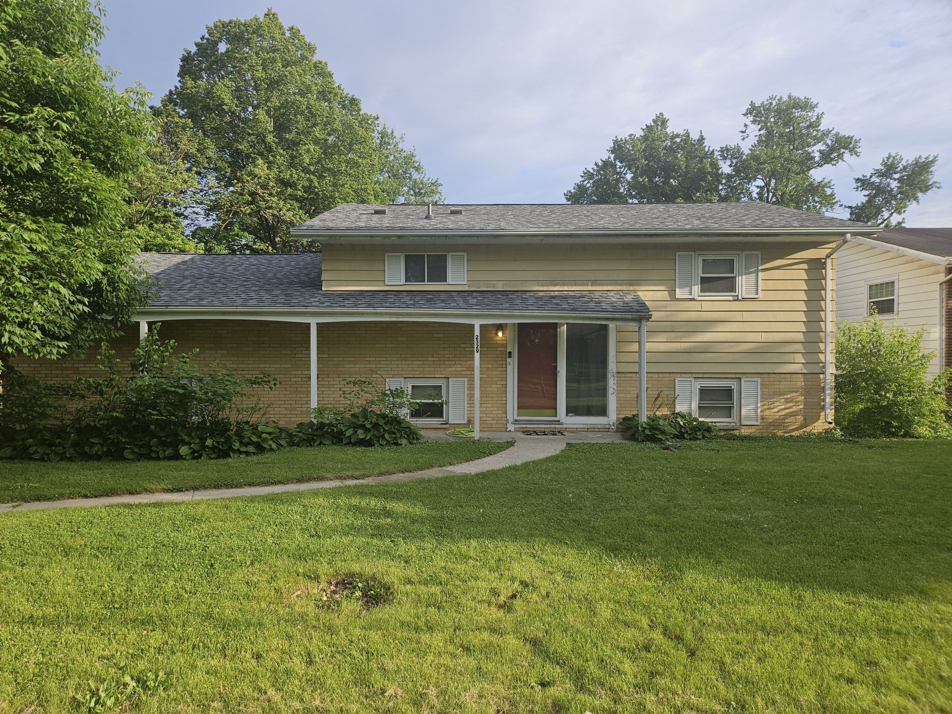 Two-story house with yellow siding and red door; lawn and trees in front.