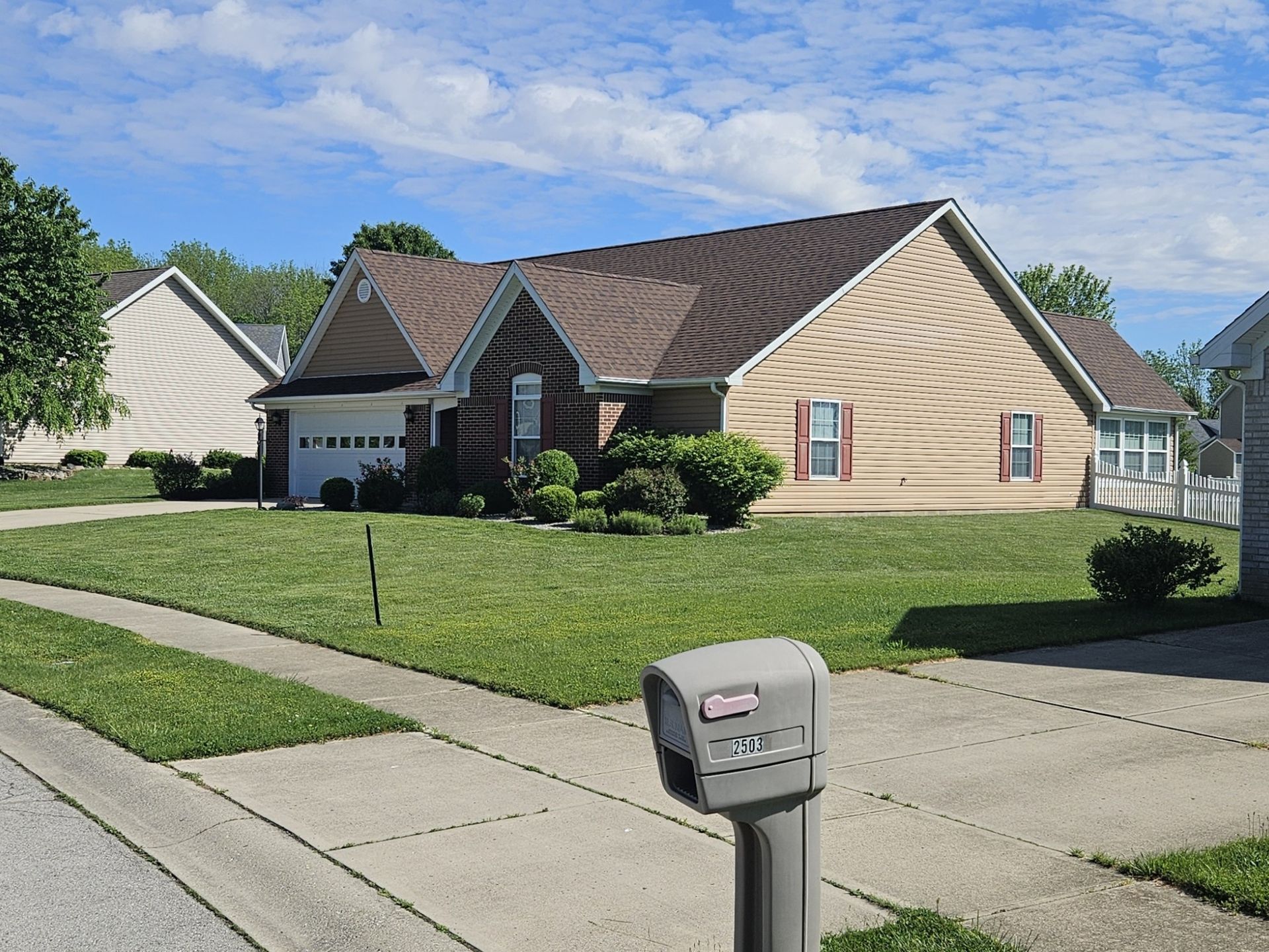 Suburban house with beige siding, brick facade, and green lawn on a sunny day.