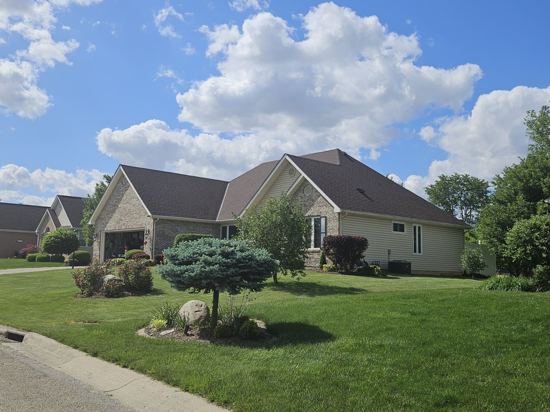 A brick house with a brown roof and a well-manicured lawn on a sunny day.
