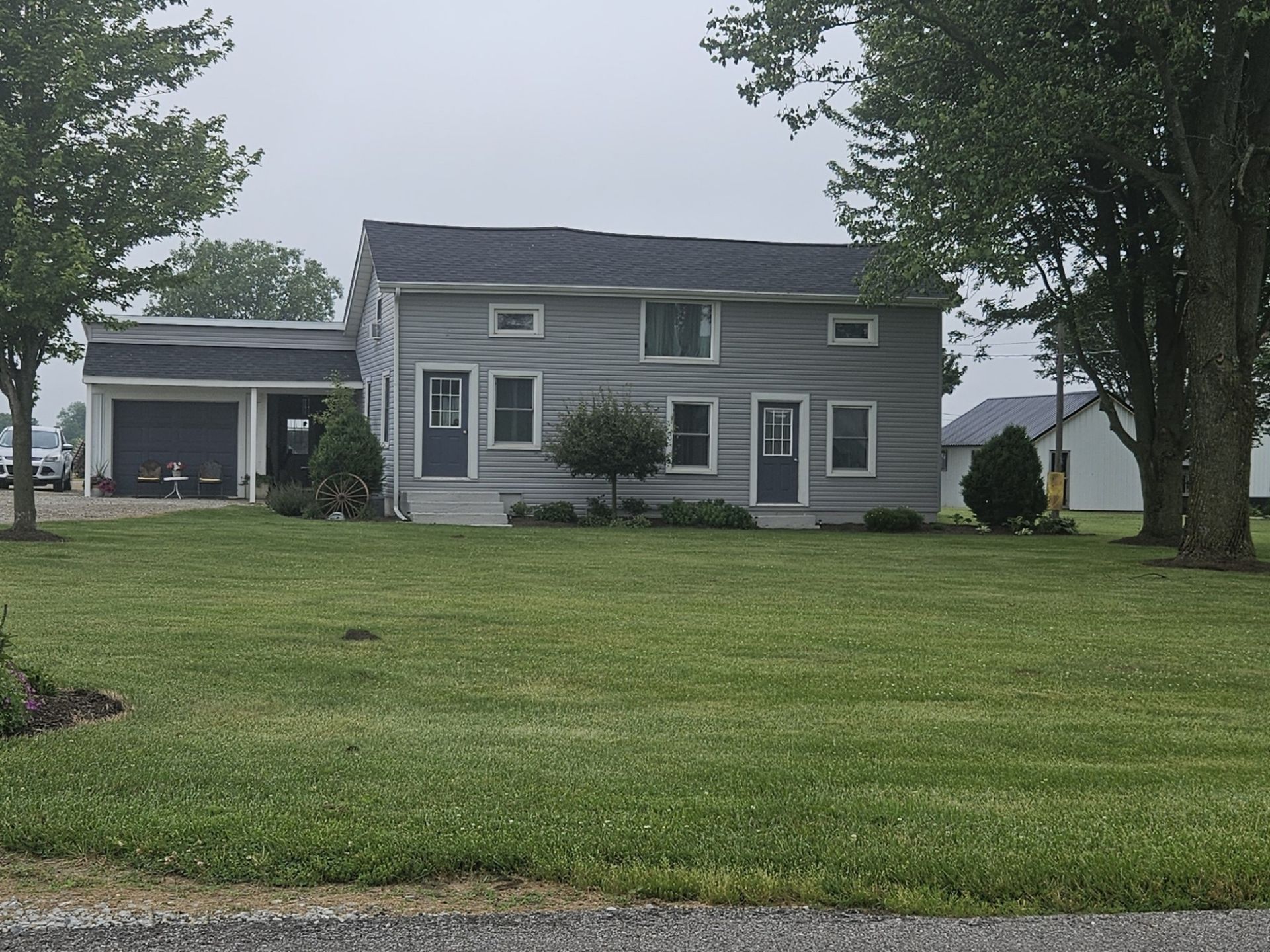 Gray two-story house with a garage, green lawn, and overcast sky.