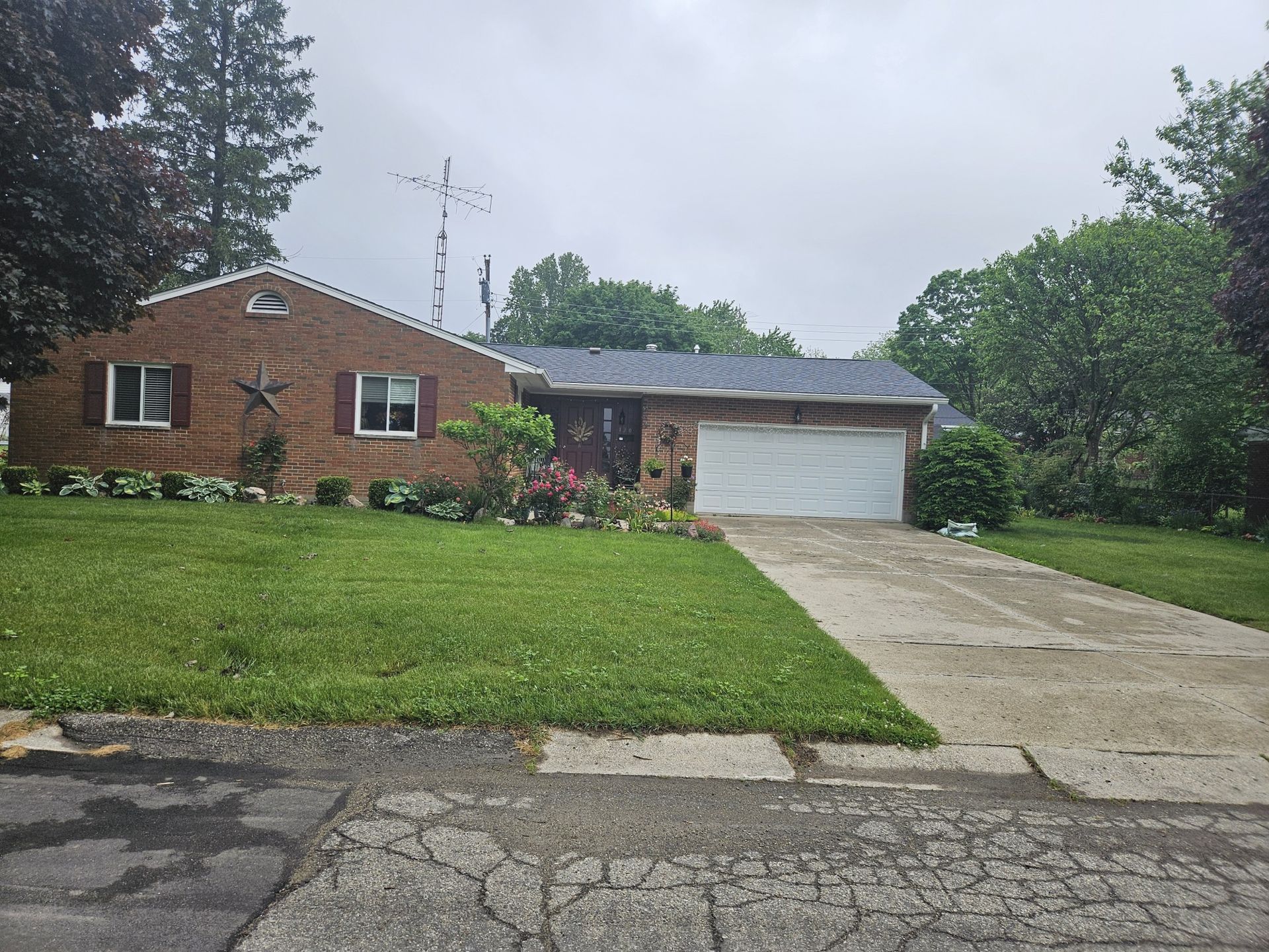 Brick house with attached garage, landscaped yard, and driveway under overcast sky.