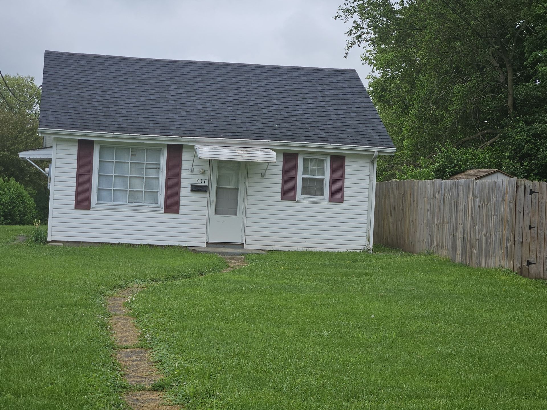 Small white house with maroon shutters and a dark roof; a wooden fence is on the right.