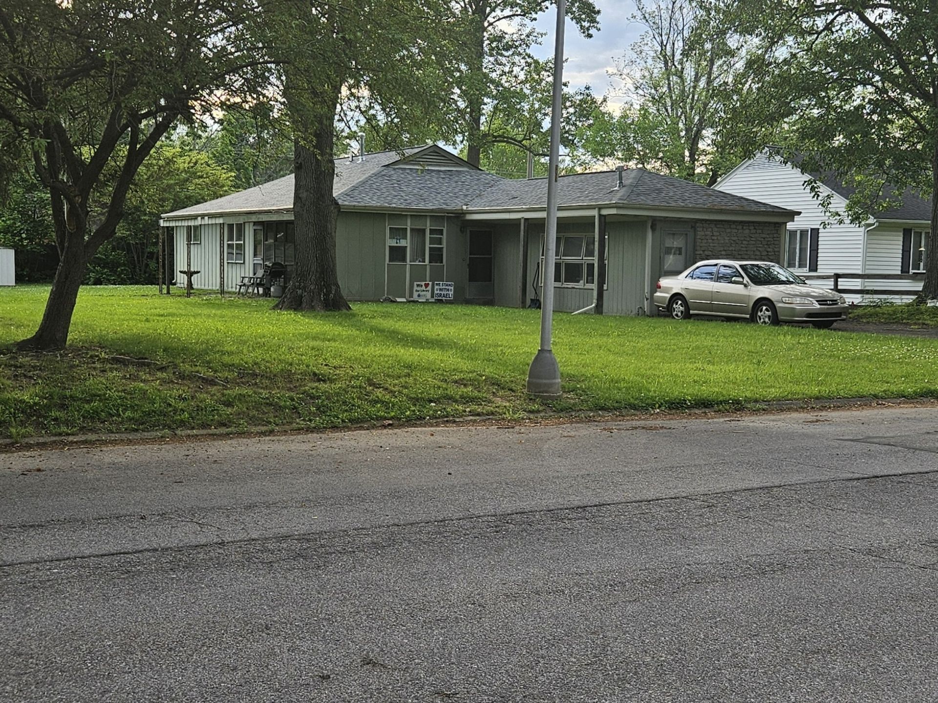 A one-story house with light green siding and a parked car on a grassy lawn.