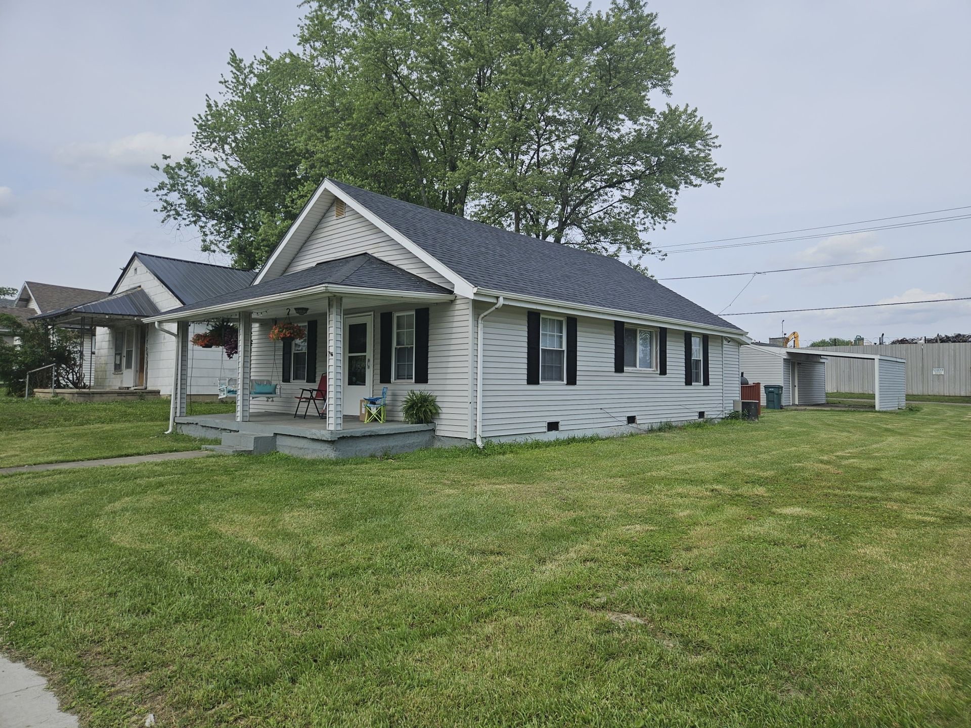 Small white house with black shutters, gray roof, and green lawn.