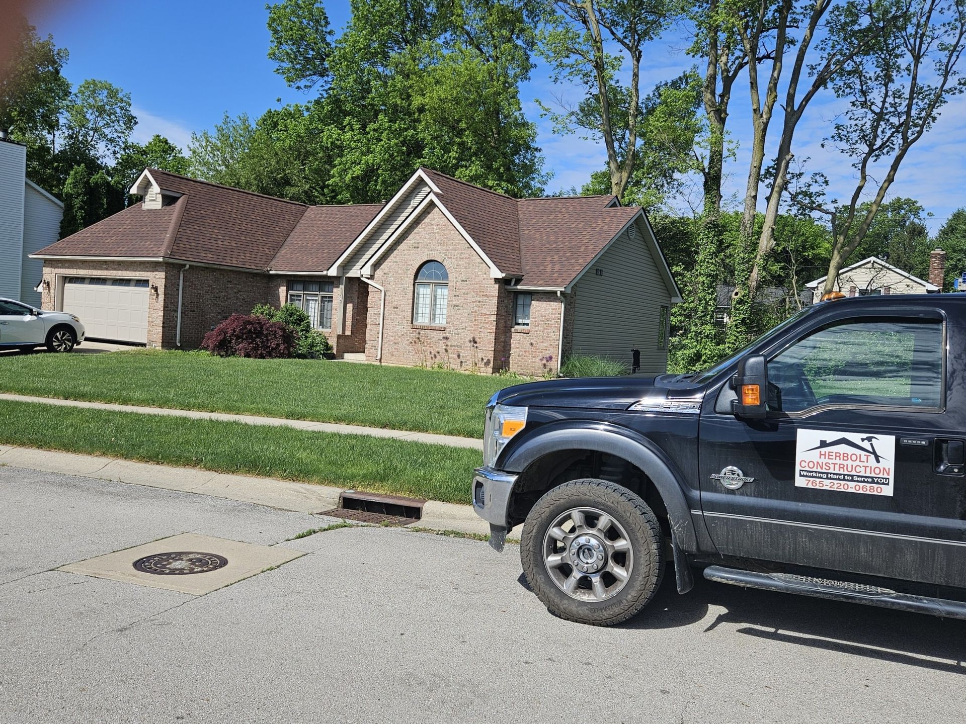 Black truck parked on street in front of a brick house with brown roof and green lawn.
