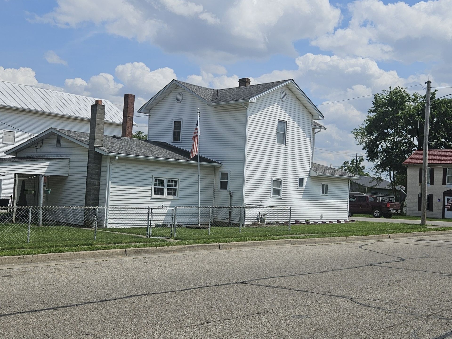 White two-story house with attached side addition; American flag flies; sunny day.