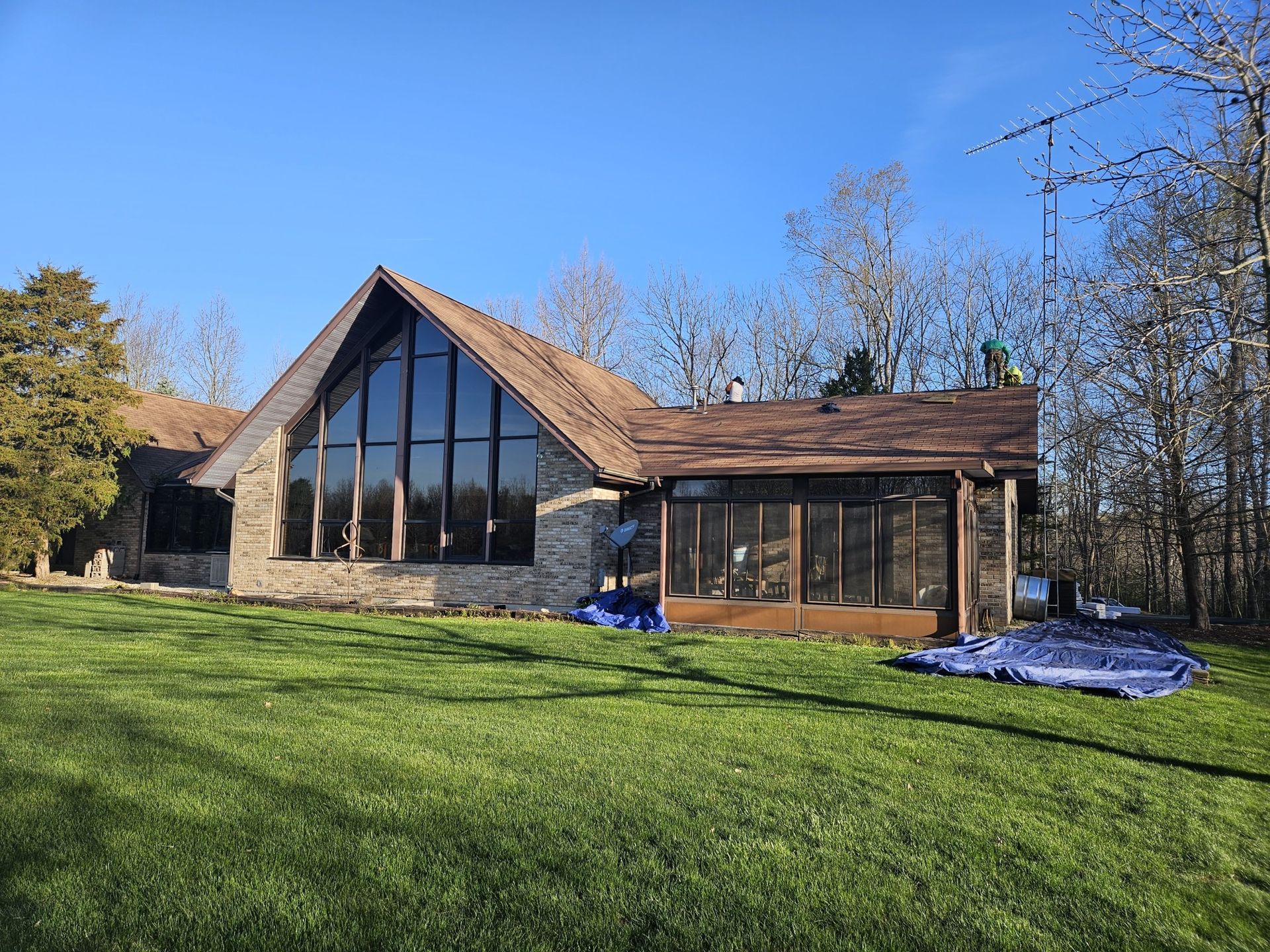 House with large windows and a brown roof surrounded by green grass and trees under a blue sky.