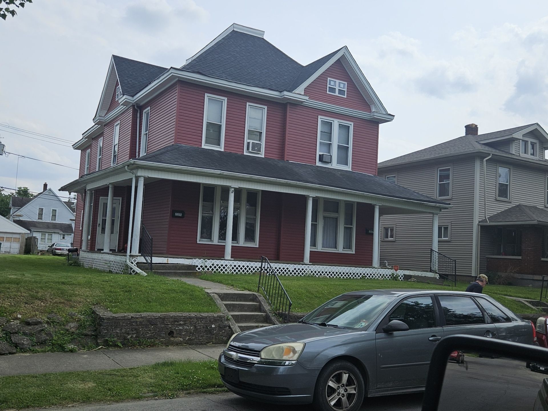 Two-story red house with white trim and a porch, a gray car in the foreground.