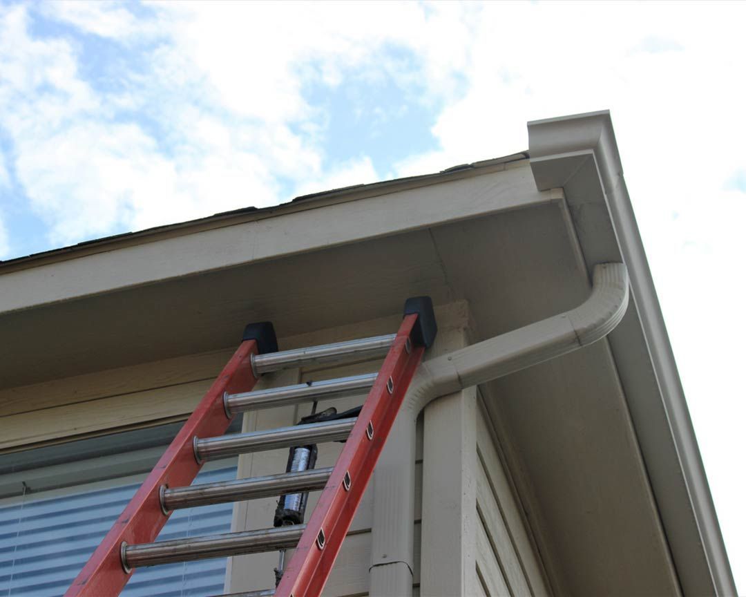 Red ladder leaning against a house with a gutter. Sky visible.