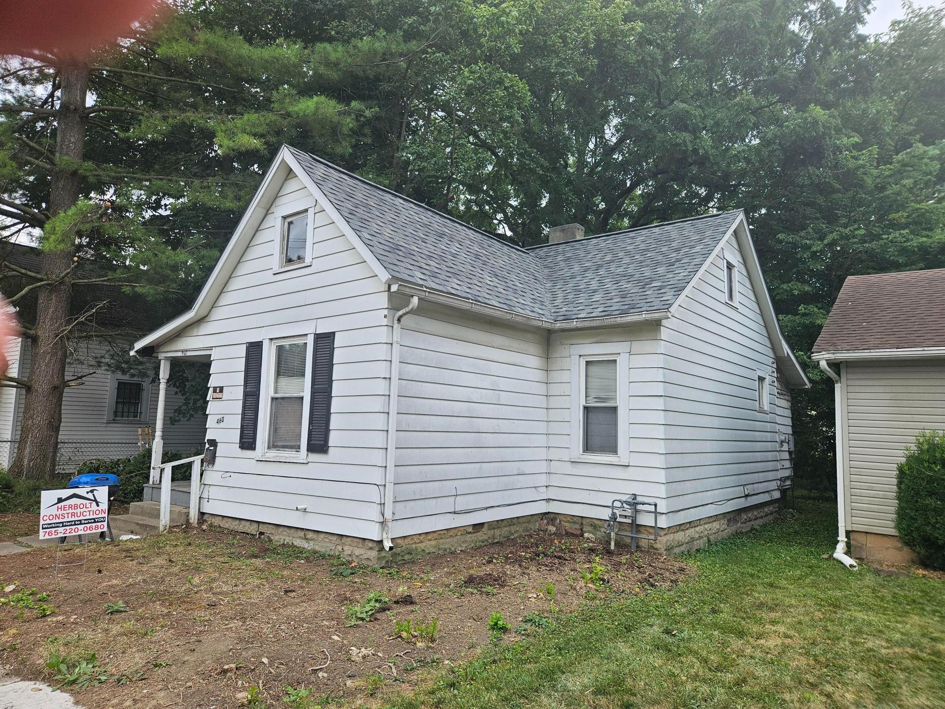 White house with dark shutters, gray roof, and small lawn. Sign in front.