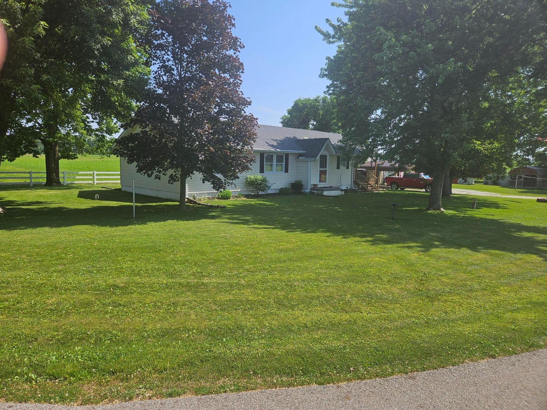 Small white house with dark roof, surrounded by trees and green lawn under a sunny sky.