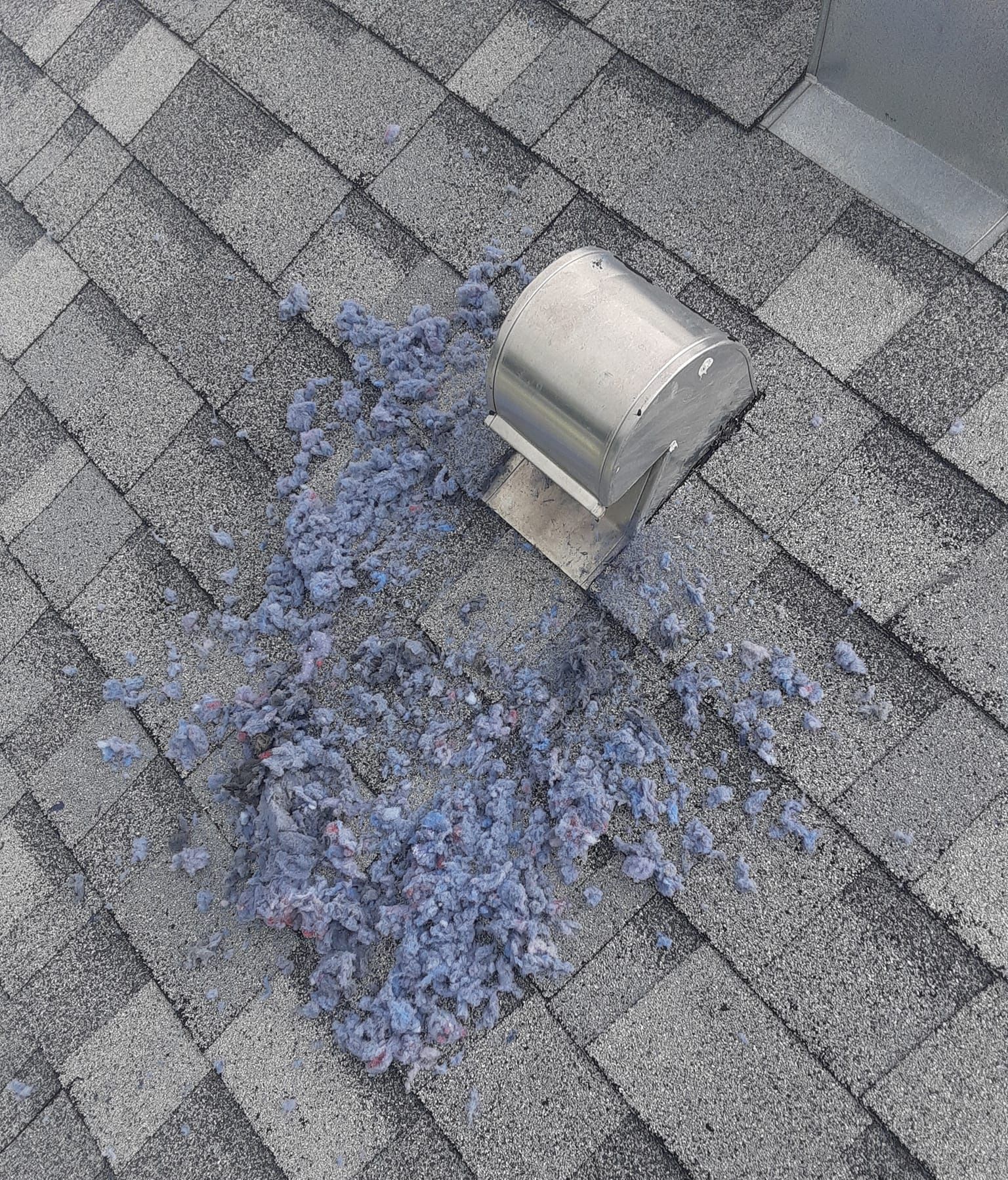 Blue insulation debris on asphalt shingle roof near a metal vent.