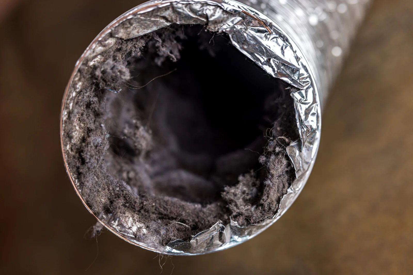Close-up of a dryer vent tube clogged with thick, dark gray lint.