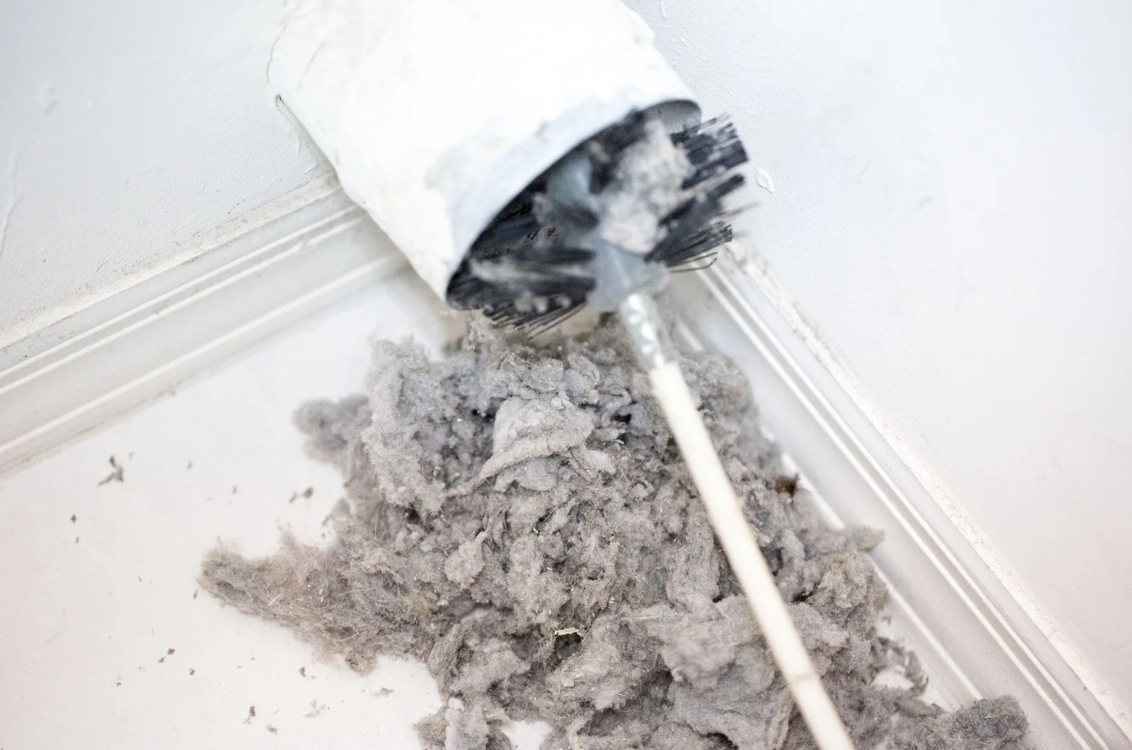 Cleaning dryer vent with brush, lint pile on floor.